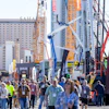 Crowded construction industry trade show with yellow and blue cranes, high-rise buildings, and attendees wearing safety gear and badges.