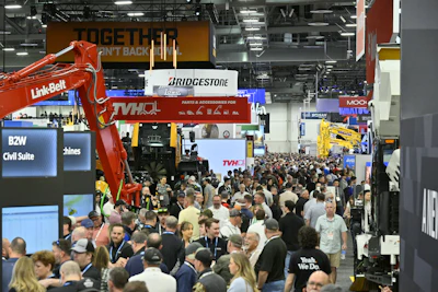 Crowded industrial trade show floor with heavy machinery, equipment displays, and multiple brand signage including Bridgestone and TVH.