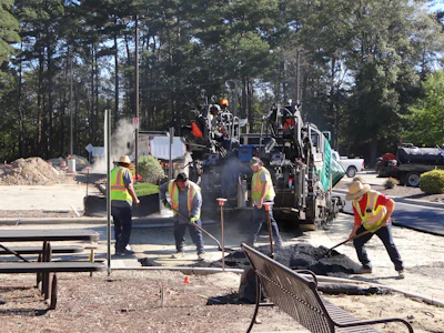 Road construction crew operating asphalt paving equipment with workers in safety vests