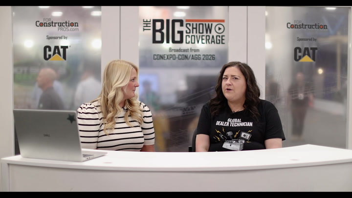 Two women at a broadcast desk during The Big Show coverage event with CAT and construction industry branding visible in background