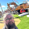 Man with beard and glasses at construction equipment trade show with SANY excavator and machinery in background