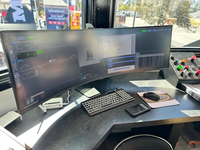Professional workstation with triple curved monitors displaying video editing software, mechanical keyboard, mouse, and control panel in bright studio setting