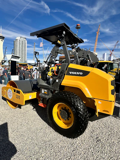 Yellow and black Volvo SD70 road roller compactor on display at construction equipment trade show with city skyline background