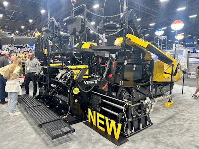 Yellow and black Versa asphalt paving machine on display at industrial trade show with visitors