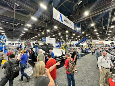 Busy trade show floor with crowds viewing industrial equipment and ASTEC branded displays under bright overhead lighting