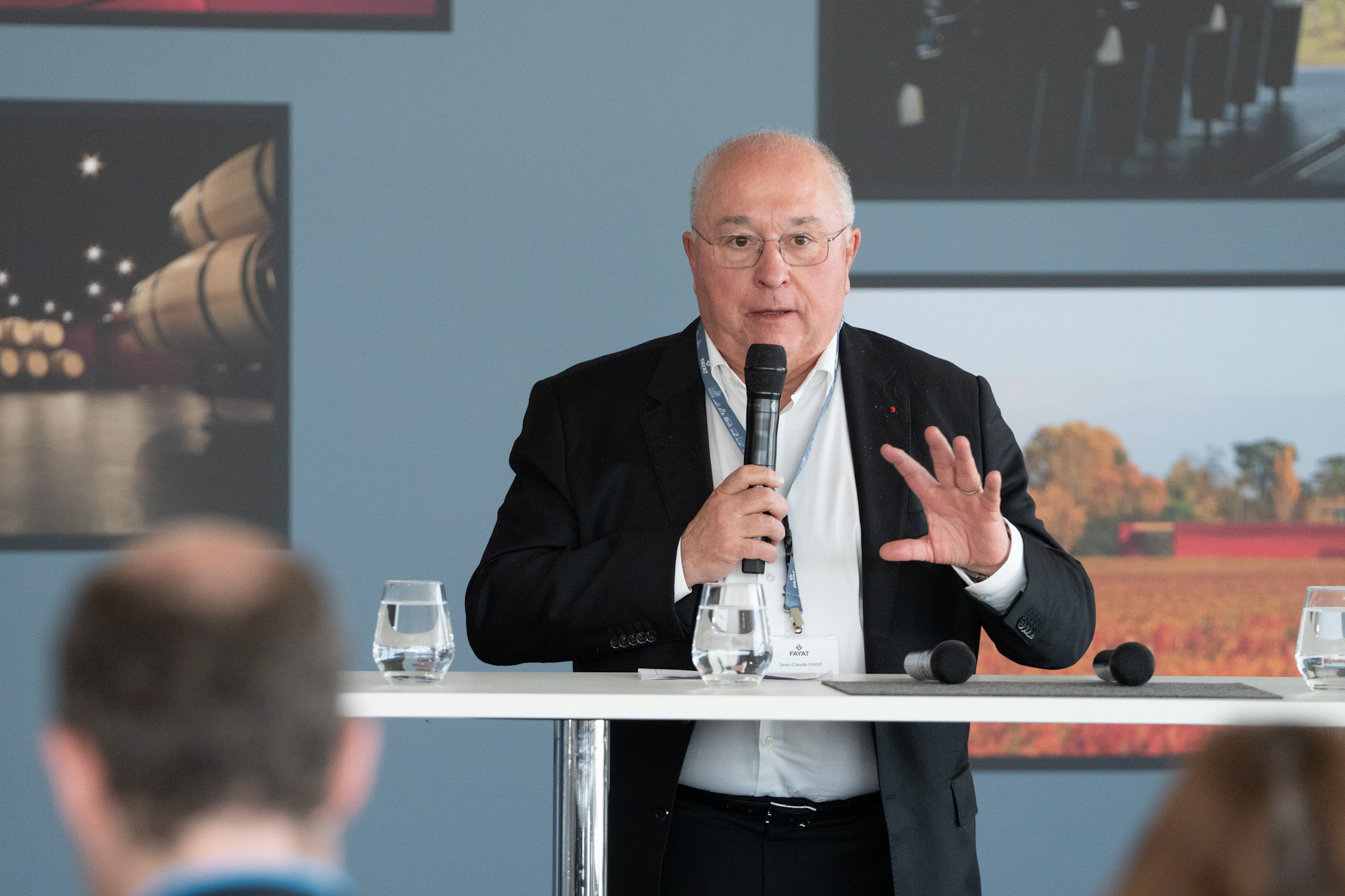 Senior professional speaking at a conference podium with microphone and water glasses