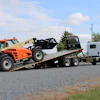 Orange JLG telehandler loaded on white flatbed tow truck on rural highway