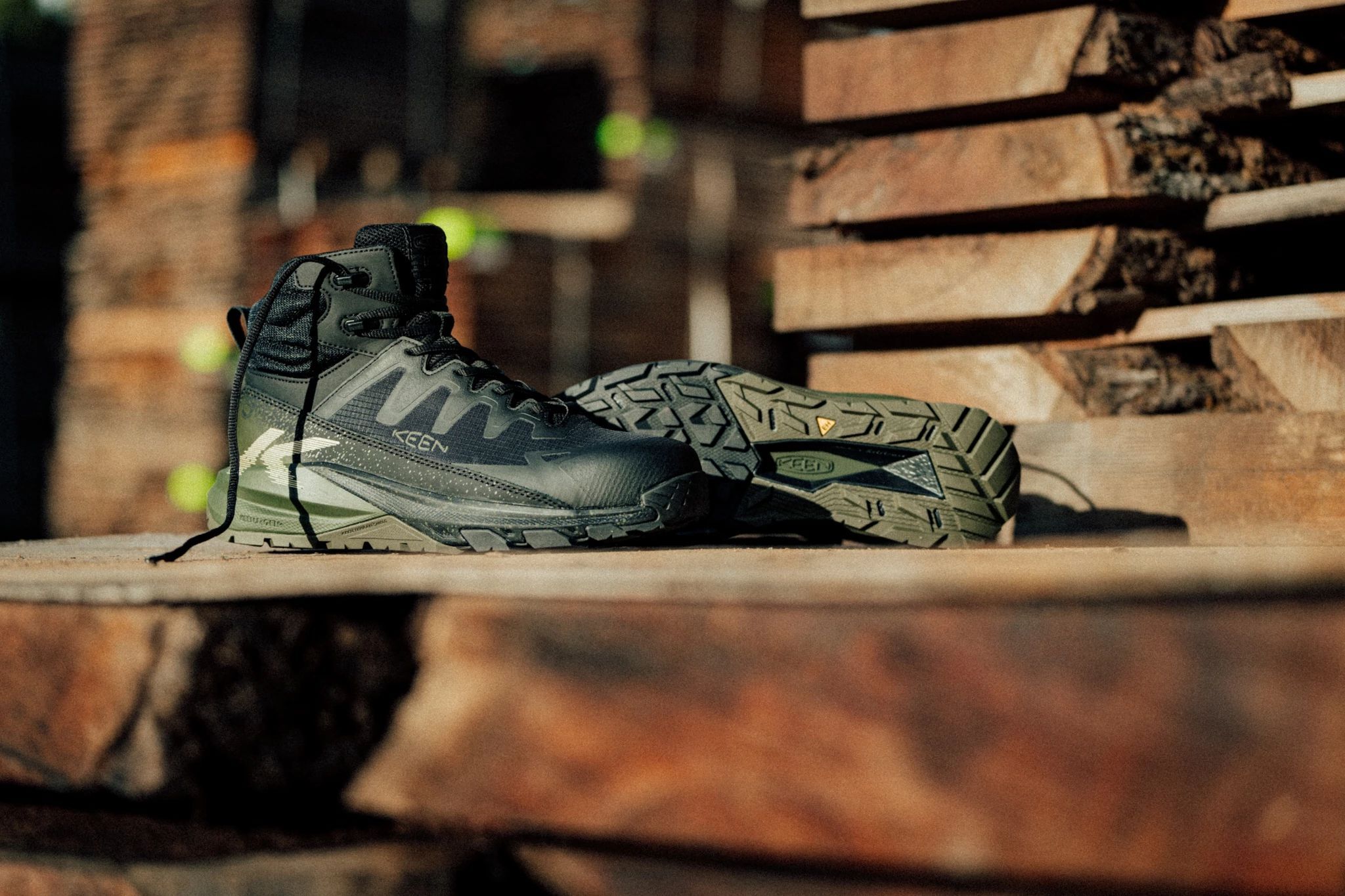 Gray and black HOKA hiking boot displayed on wooden logs in outdoor setting