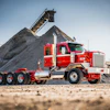 Red and white Peterbilt truck positioned at aggregate quarry with conveyor system and gravel pile in background