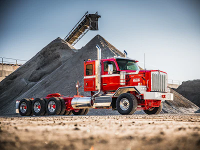 Red and white Peterbilt truck positioned at aggregate quarry with conveyor system and gravel pile in background