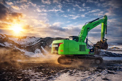 Bright green LIUGONG excavator operating on snowy terrain at sunset with dramatic sky