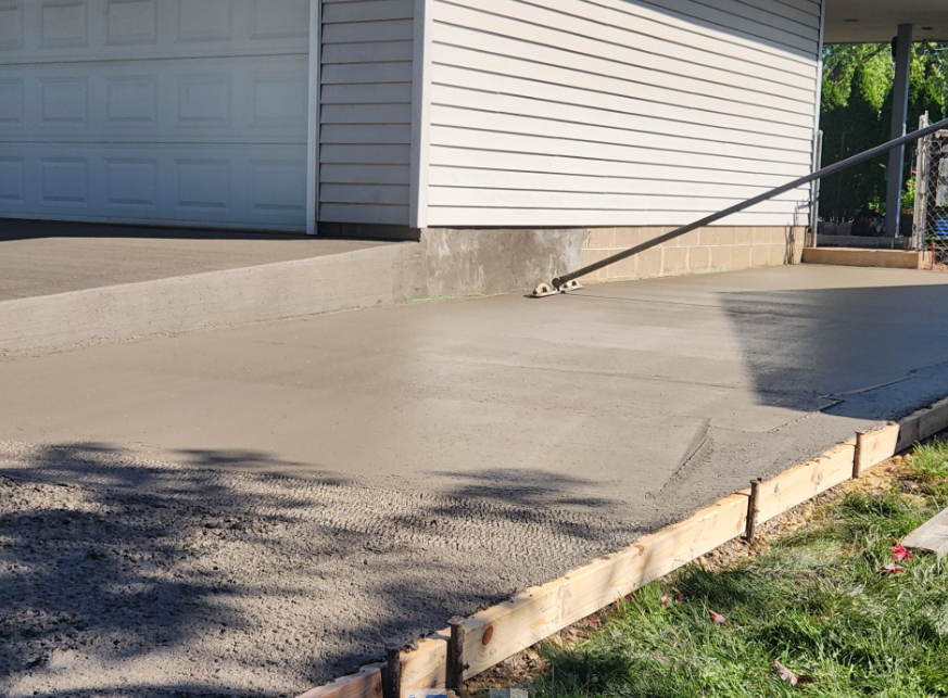 Newly poured concrete driveway with wooden forms and white garage doors visible