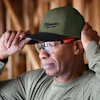Man wearing green Milwaukee baseball cap and safety glasses in workshop setting