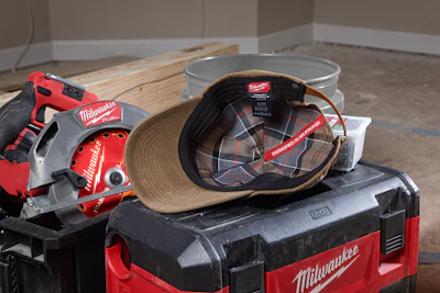 Milwaukee power tools and equipment arranged on red toolbox with hard hat and wooden boards