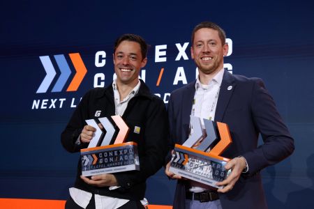 Two men in business attire holding awards at a CXGA conference event with branded backdrop