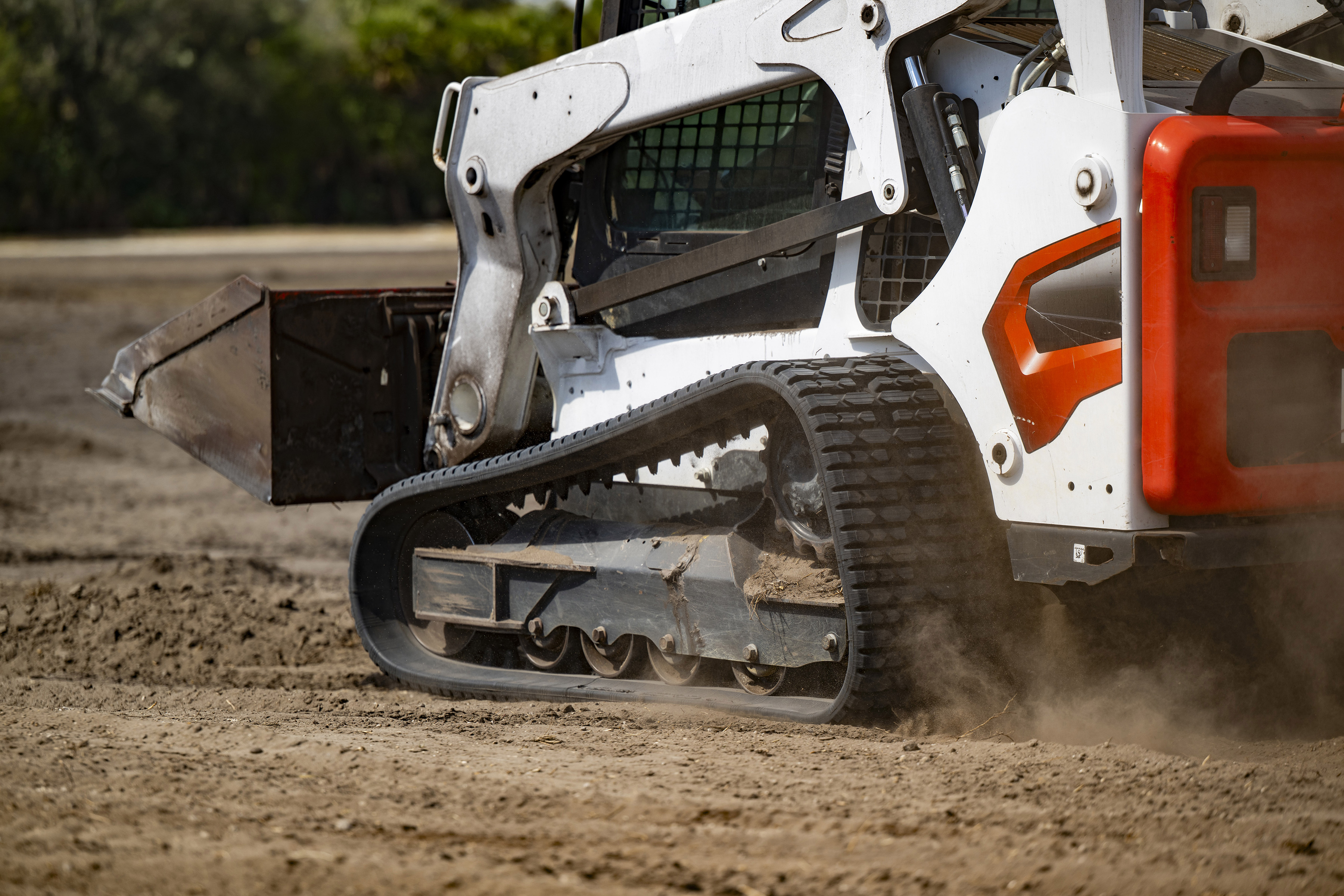 White and orange skid steer loader spreading dirt on construction site