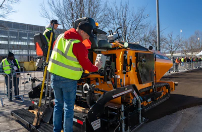 Construction workers operating orange tracked snow removal equipment at outdoor winter event