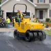 Construction worker operating a yellow SAKAI road roller compactor on a residential driveway during paving work