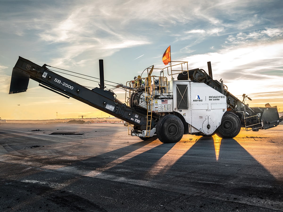 ROADTEC asphalt paving machine operating on a road at sunset with dramatic sky