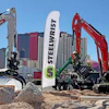 Heavy construction equipment display with Steelwrist branded banner and excavators on sandy ground
