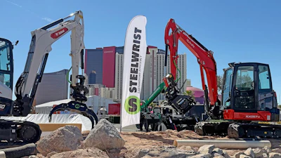 Heavy construction equipment display with Steelwrist branded banner and excavators on sandy ground