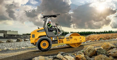 Yellow Volvo road roller compacting gravel at construction site under cloudy sky