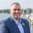 Professional man in navy blazer smiling at marina with sailboats in background Headshot