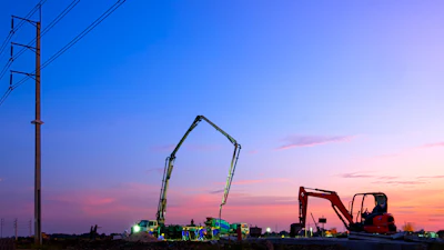 Construction equipment silhouetted against twilight sky with power lines and colorful sunset clouds