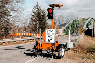 Portable traffic control sign on orange trailer with red light and stop instructions near bridge