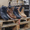 Four work boots in navy, brown, and tan displayed on wooden pallet in industrial setting
