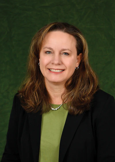 Professional headshot of a woman in business attire smiling against a green background