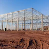 Large steel-frame greenhouse structure under construction on bare earth with clear blue sky