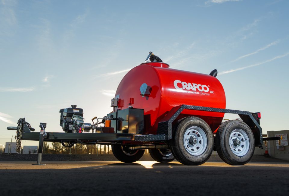 Red CRAFCO tanker trailer with dual axles parked in industrial yard under clear sky