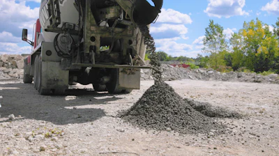 Concrete mixer truck discharging aggregate at construction site with stockpiles and trees