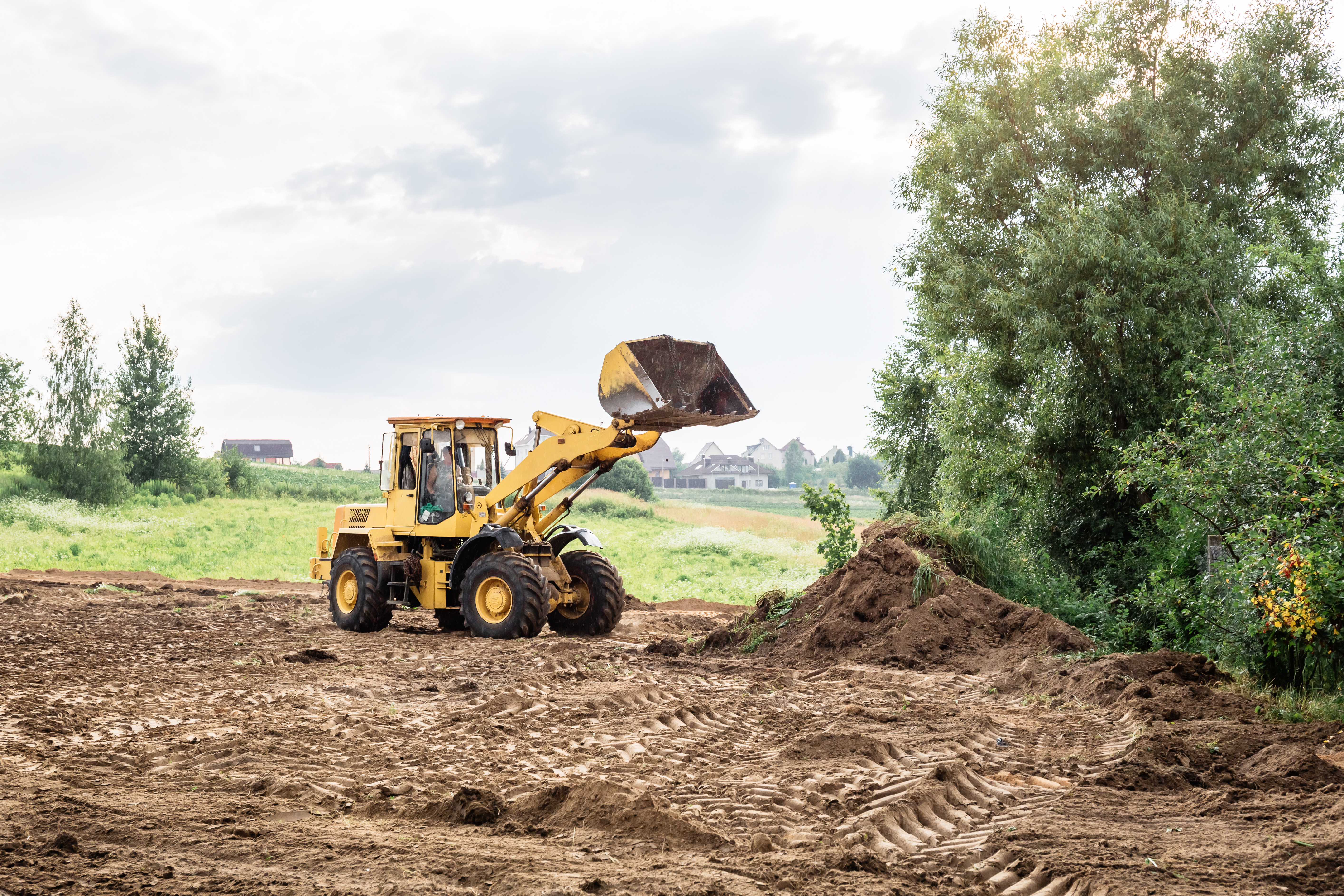 Yellow wheel loader scooping soil at construction site with rural landscape and trees in background