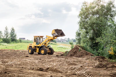 Yellow wheel loader scooping soil at construction site with rural landscape and trees in background