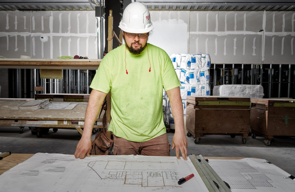 Construction worker in safety gear reviewing building blueprints at a workbench in a garage.