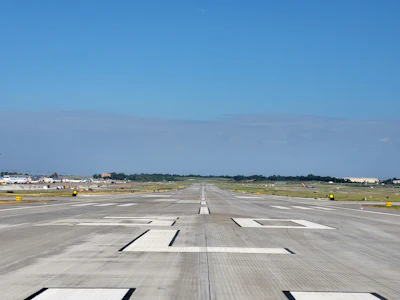 Empty airport runway stretching into distance with clear blue sky and taxiway markings visible