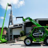 Bright green Merlo telehandler with extended boom positioned outside modern industrial building