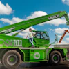 Green Merlo telescopic handler with operator on construction site under blue sky