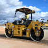 Yellow CAT CB13 asphalt roller compactor with operator on construction site under blue sky