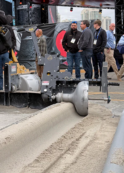 Industrial soil compactor machine displayed at outdoor trade show with attendees in hard hats observing the equipment