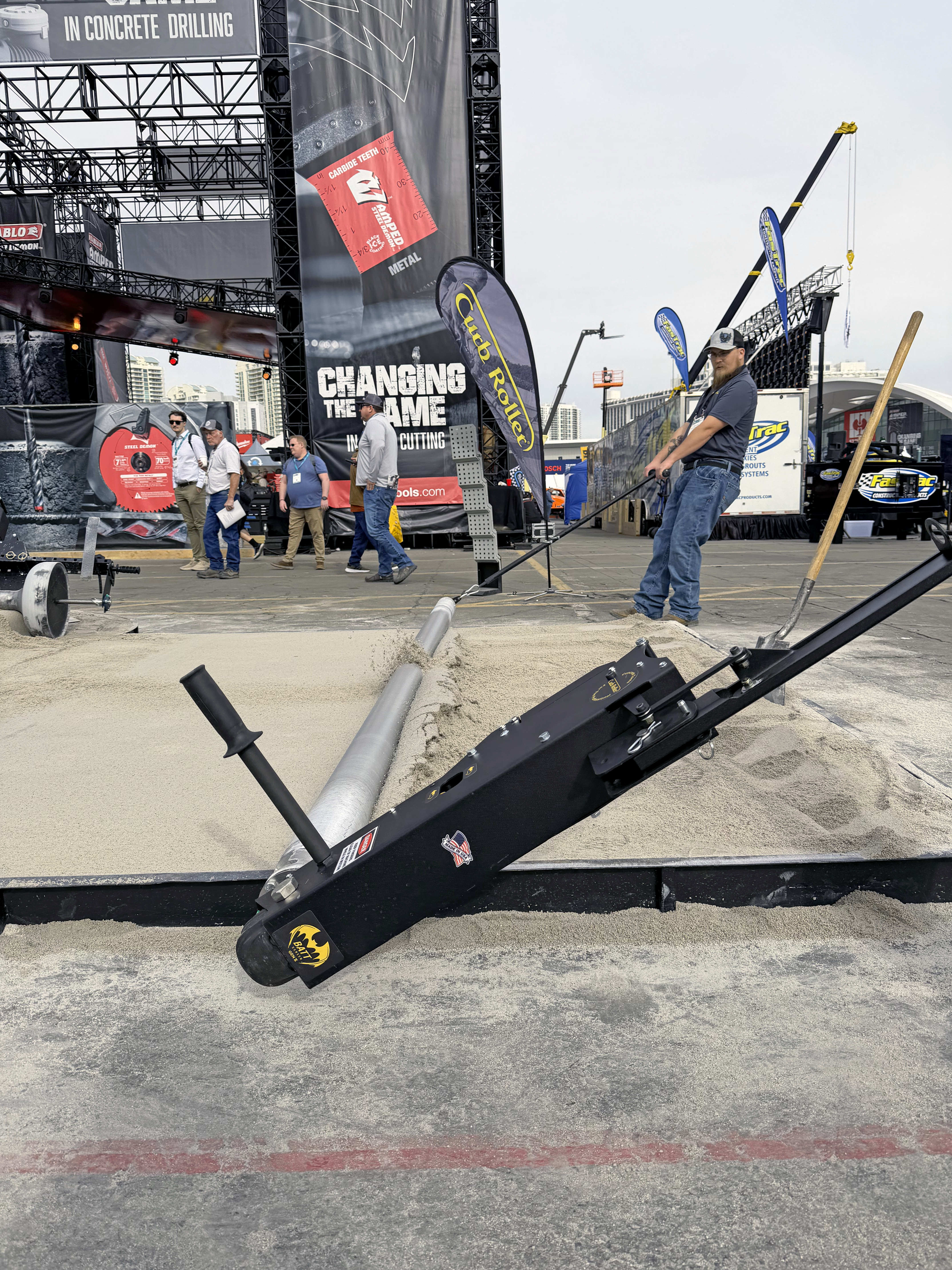 Concrete drilling equipment demonstration at outdoor trade show with spectators and branded signage in background