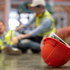 Red hard hat in foreground with construction workers in safety vests on industrial site