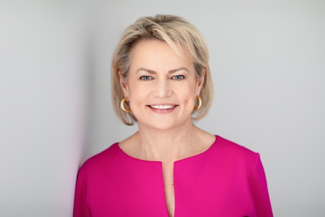 Professional headshot of a smiling woman with blonde hair wearing a magenta blouse
