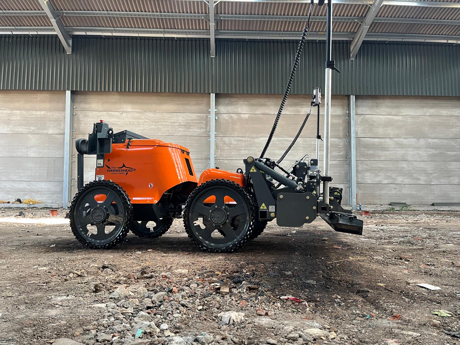 Orange and black agricultural tractor with attached hydraulic implement in industrial yard