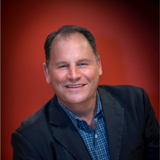 Professional headshot of a smiling man in business casual attire against a red background Headshot