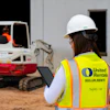 Construction worker wearing United Rentals safety vest and hard hat operating excavator on job site