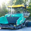 Turquoise VÖGELE asphalt paver with yellow crane attachment parked outdoors near trees