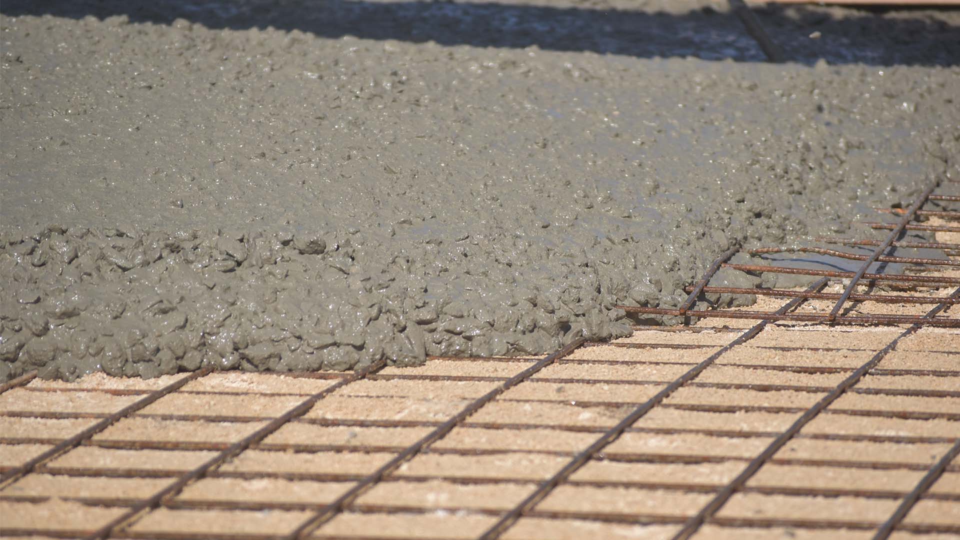 Wet concrete being poured over metal reinforcement mesh during construction flooring work